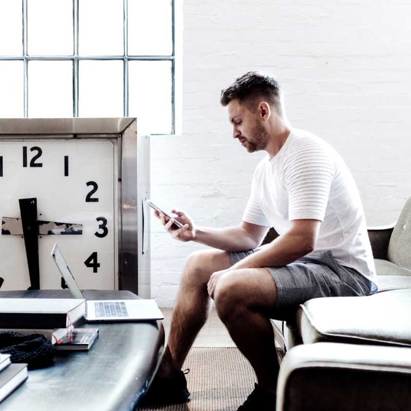 Man sitting on a sofa looking at a phone with a clock in the background